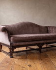 Three-quarter view of the camelback sofa showing the pleated scroll arm, tufted arm, fretwork legs and stretcher