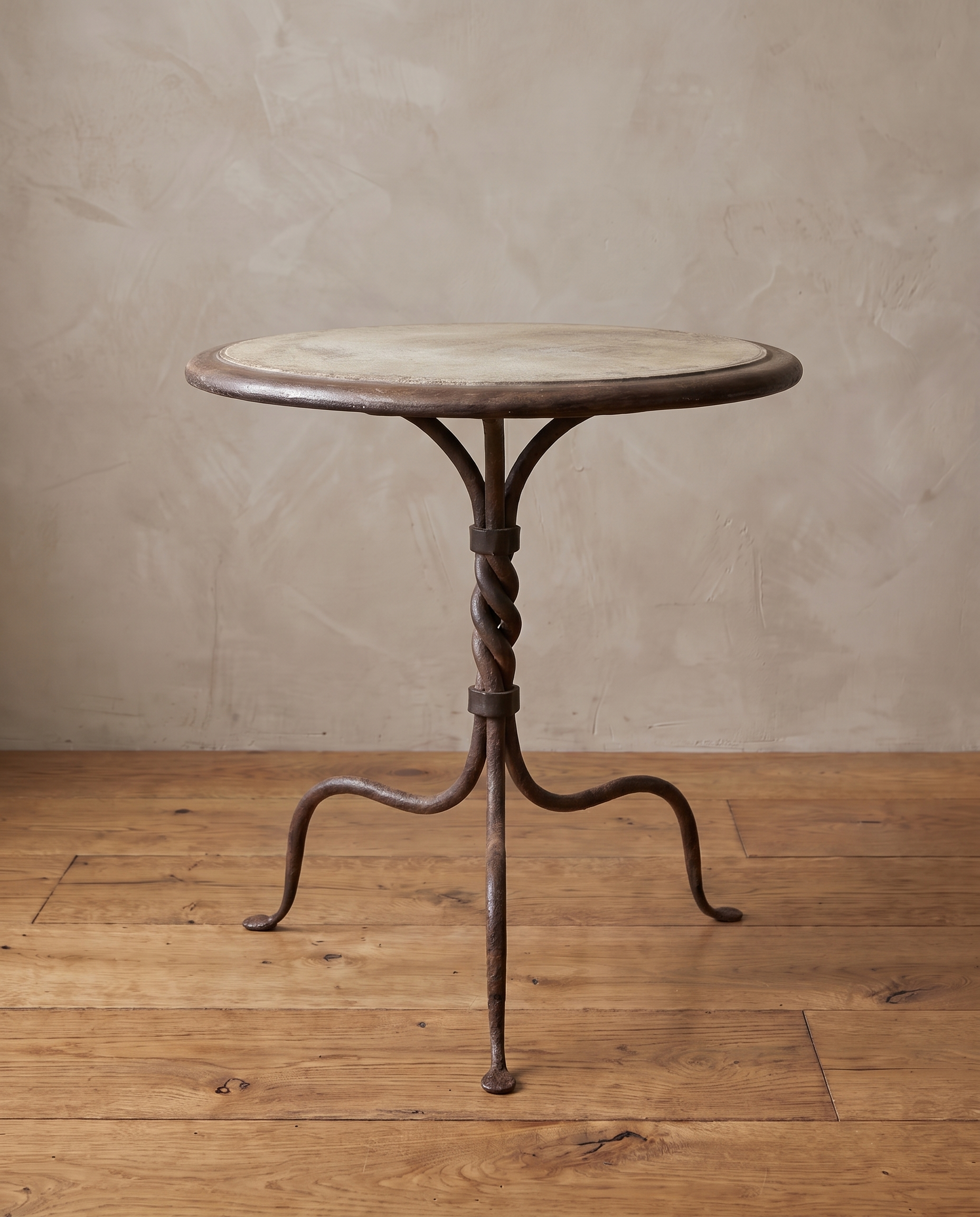 Vintage cement bistro table with twisted wrought iron tripod base against a greige plaster wall on a reclaimed wood floor