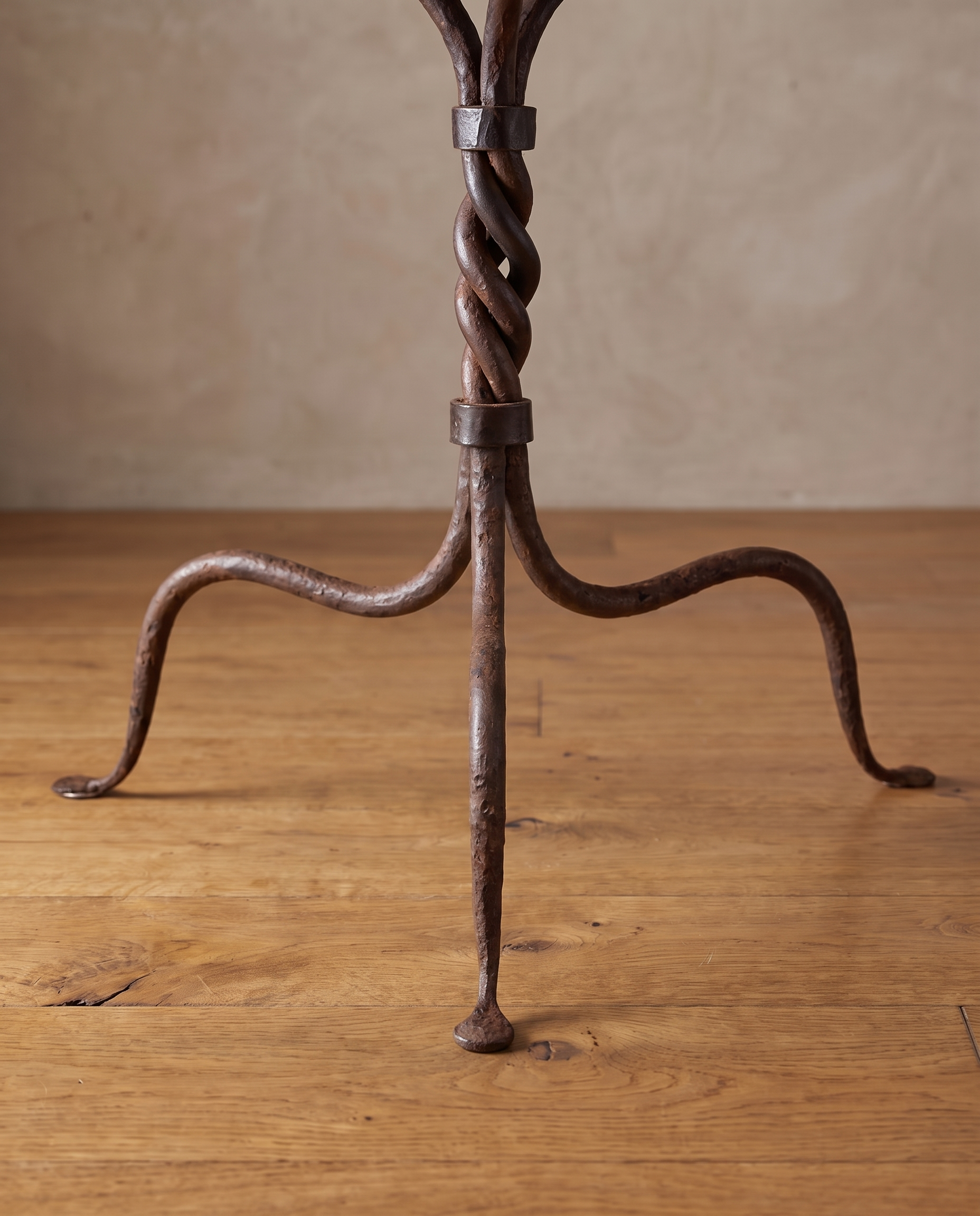 Three evenly spaced curved iron legs with pad feet on a reclaimed wood floor