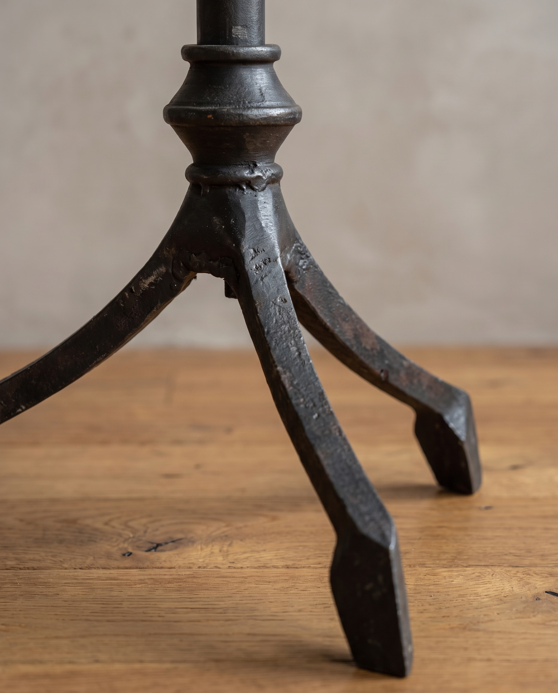 Close-up of the forged iron tripod base with three splayed legs and spade feet on a reclaimed wood floor