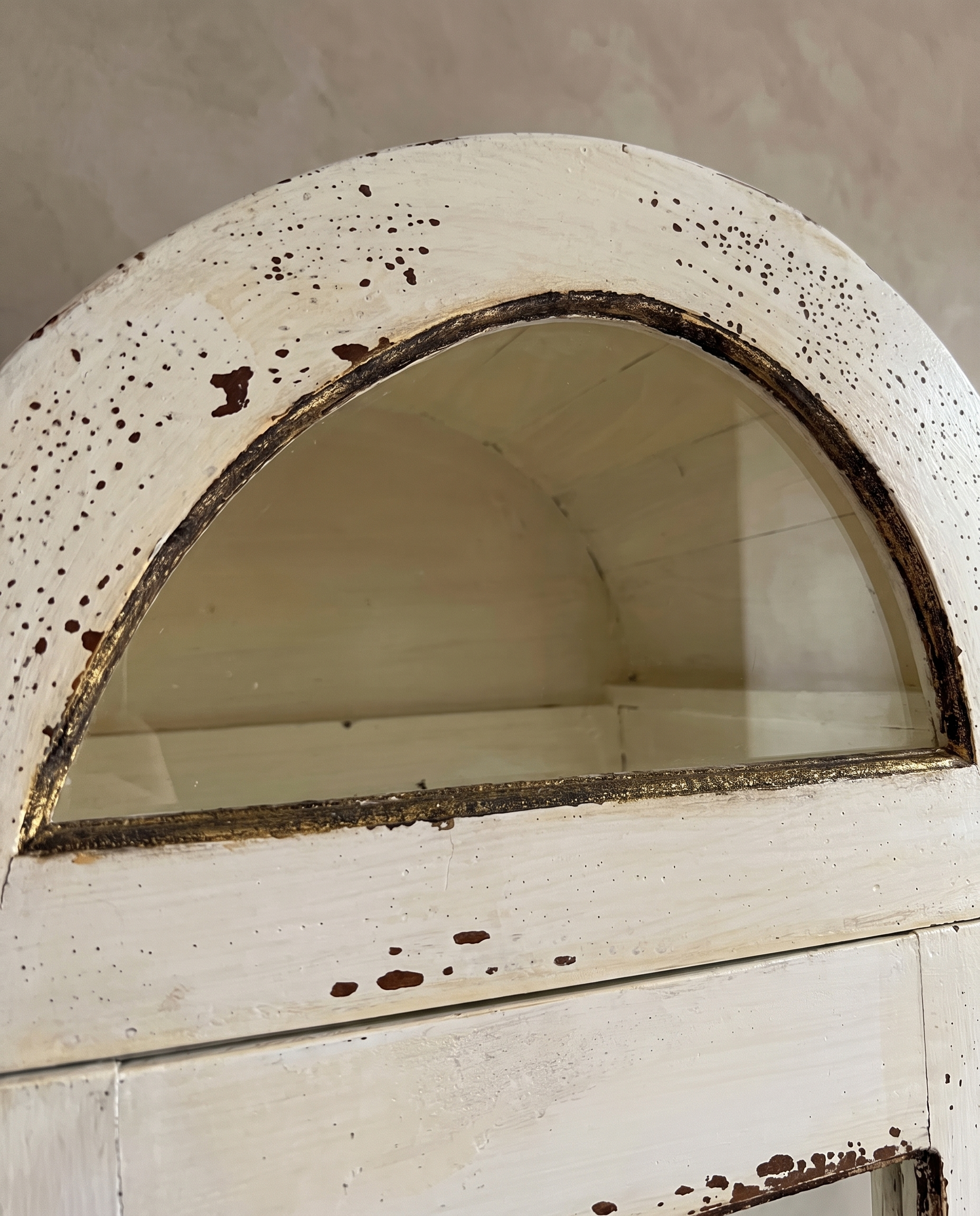 Close-up of the arched top with half-moon glass and speckled distressed cream paint