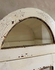 Close-up of the arched top with half-moon glass and speckled distressed cream paint