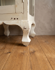 Carved cabriole legs and scalloped apron of the cabinet on a reclaimed wood floor