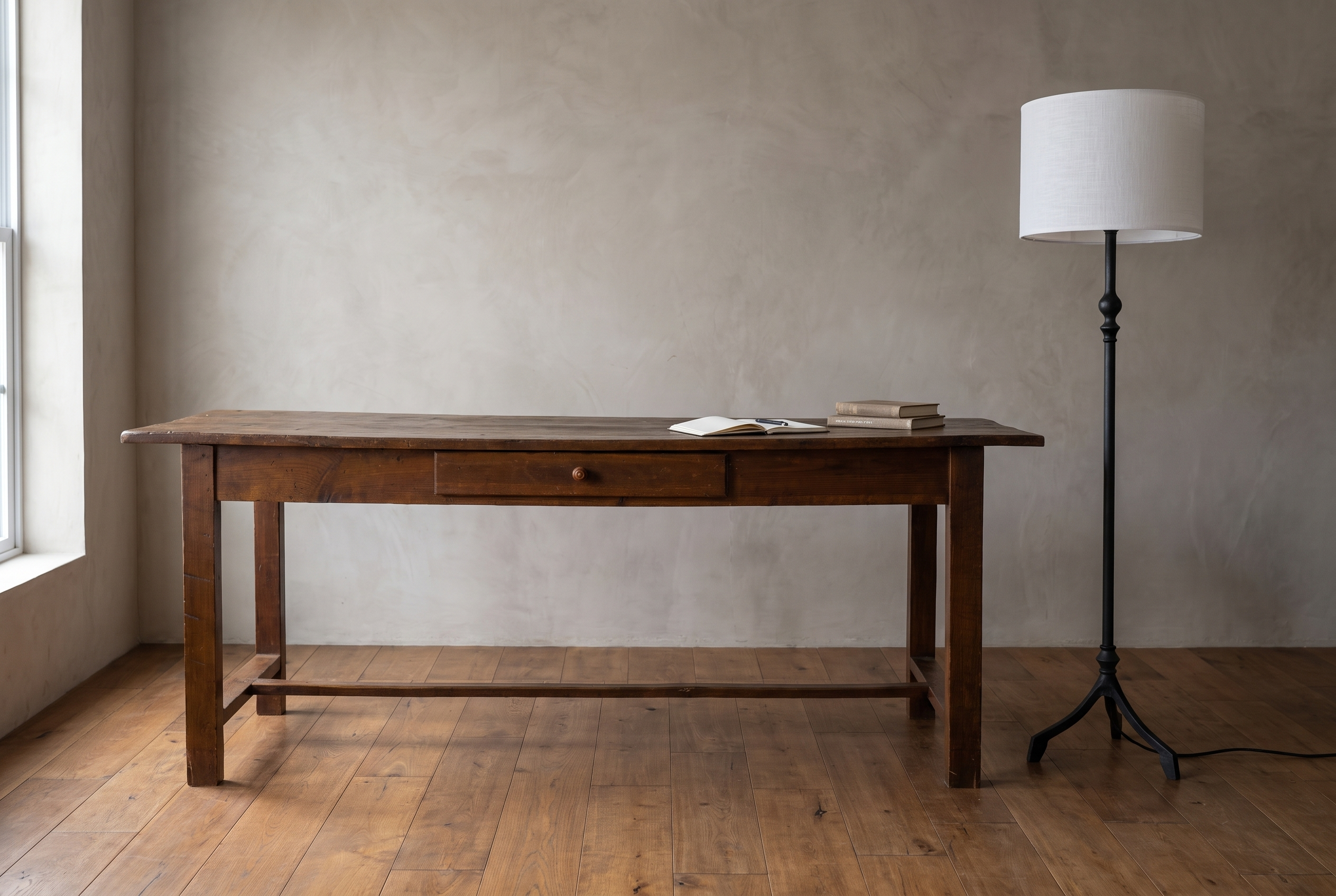 Forged iron tripod floor lamp beside a long antique farmhouse writing desk, plaster wall and reclaimed wood floor