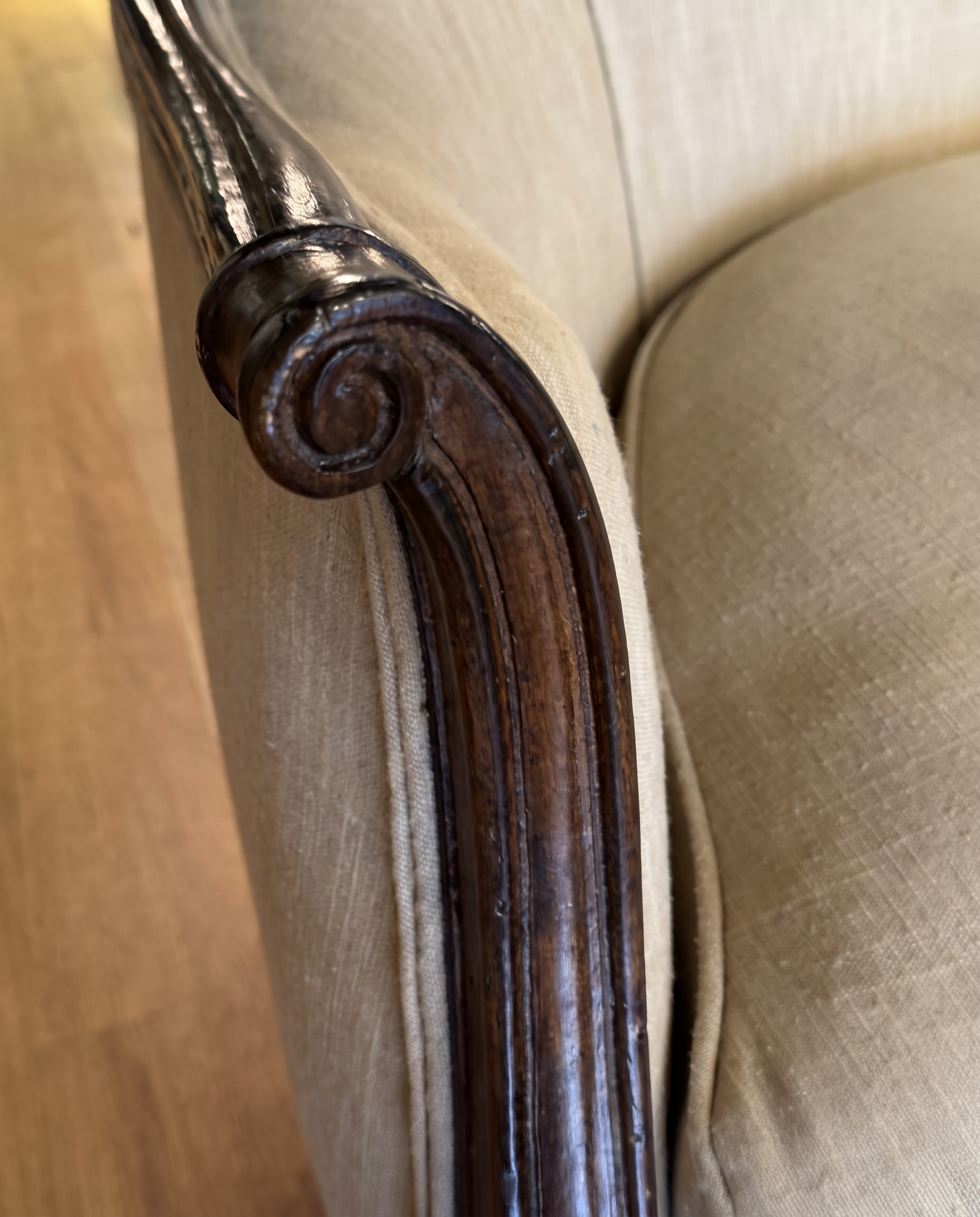 Close-up of the carved scroll at the end of the settee arm beside the oatmeal linen