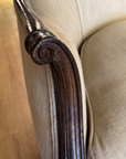 Close-up of the carved scroll at the end of the settee arm beside the oatmeal linen