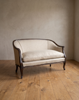 Angled view of the Trianon settee showing its barrel back, scrolled arms and cabriole legs