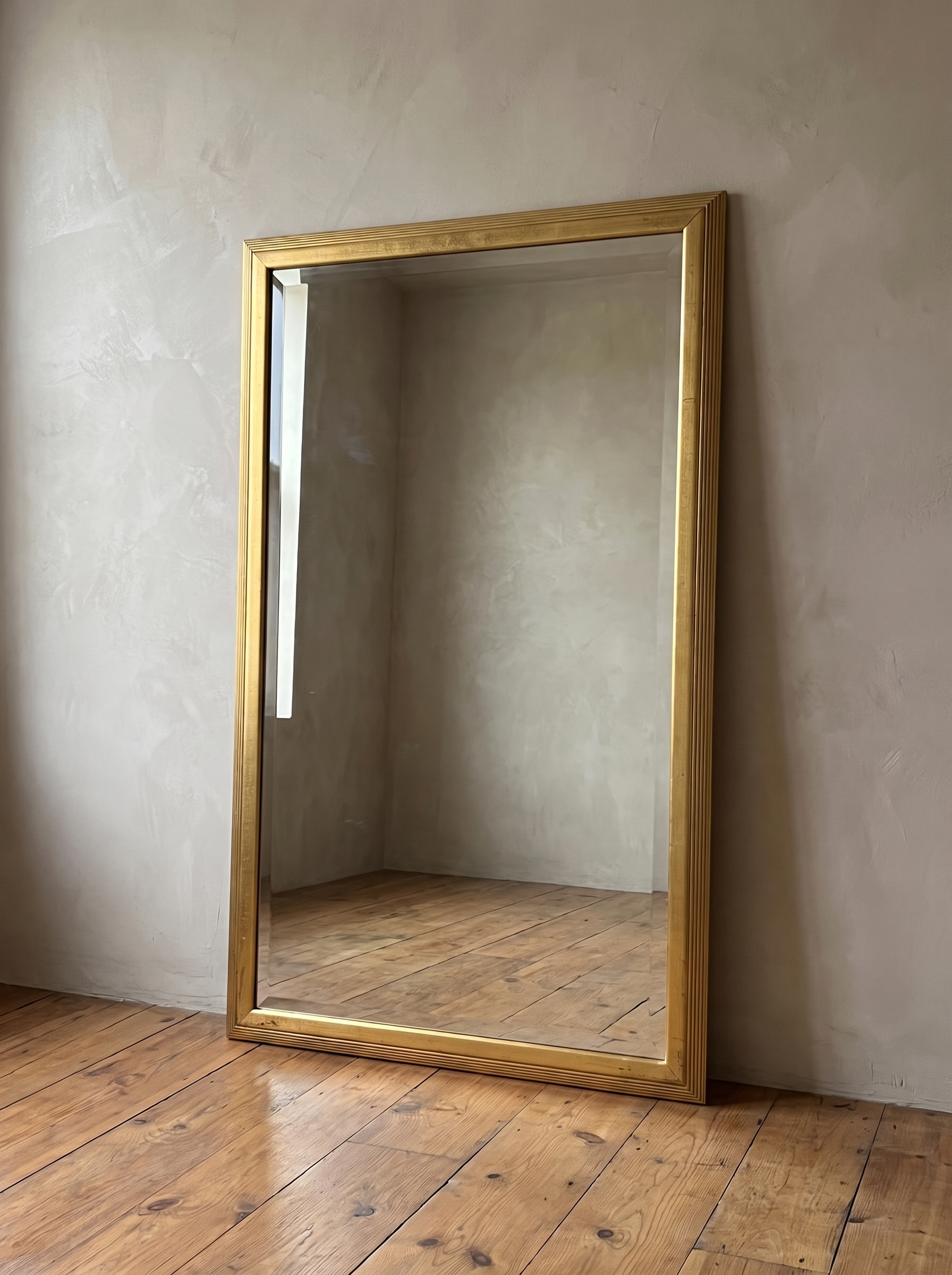 Gilt reeded wood mirror leaning against a warm plaster wall on a reclaimed wood floor