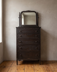 Antique five-drawer chest with arched swing mirror against a warm plaster wall on a reclaimed wood floor