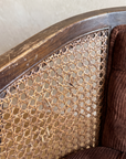Close-up of the curved walnut arm, woven cane with natural wear, and tufted ribbed velvet