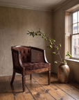 Vintage cocoa velvet cane barrel chair in a plaster-walled apartment beside a wood-fired jar with a fruiting branch