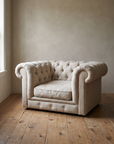 Natural linen tufted chesterfield chair-and-a-half, three-quarter view, against a warm plaster wall on a knotted reclaimed wood floor