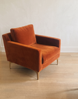 Rust velvet armchair, three-quarter view, on a light oak floor