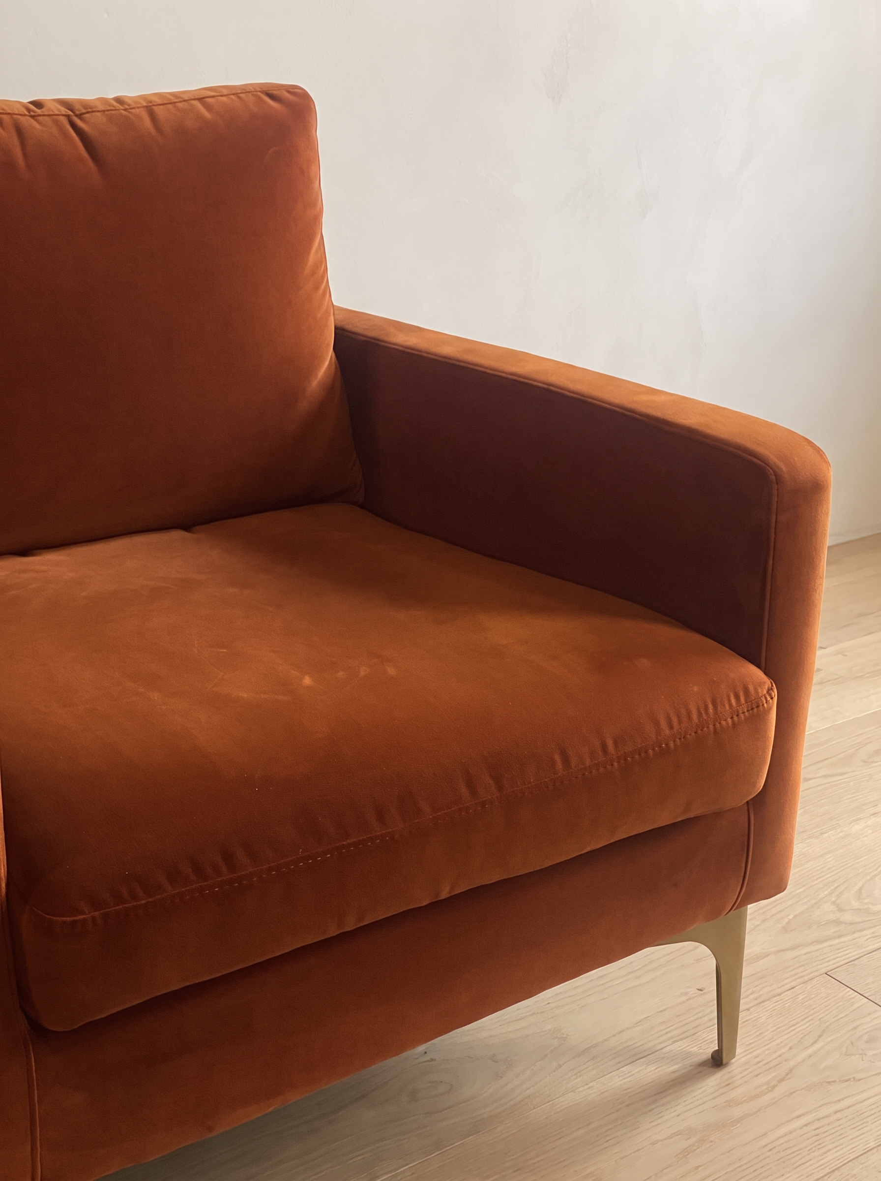 Close-up of the rust velvet seat cushion, arm and brass leg