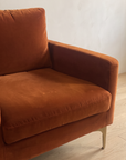 Close-up of the rust velvet seat cushion, arm and brass leg