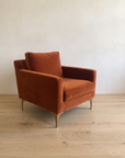 Rust velvet armchair, close three-quarter view showing track arm and brass legs