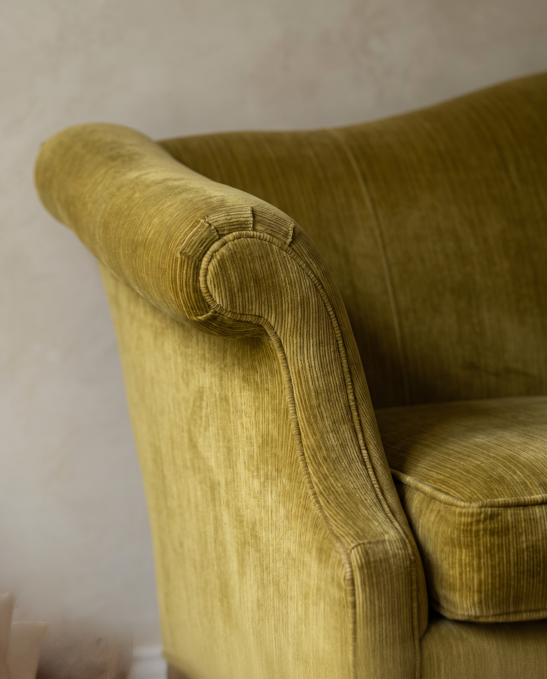 Detail of the scroll arm flaring outward in olive chartreuse velvet