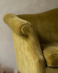 Detail of the scroll arm flaring outward in olive chartreuse velvet