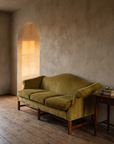 Vintage chartreuse velvet camelback sofa in a plaster room, golden light through an arched doorway