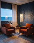 Two rust velvet armchairs with a wood slab side table under a glowing netted floor lamp in a dusky blue plaster room