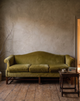 Close view of the chartreuse camelback sofa beside an antique side table