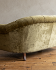Finished rounded back of the olive velvet sofa with brass nailheads