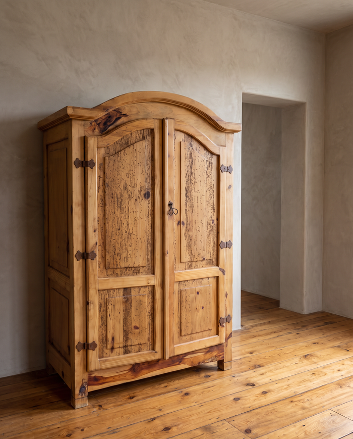 Handmade Mexican pine bonnet-top armoire against a greige plaster wall on a reclaimed wood floor