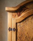 Close-up of the arched cornice with a swirled pine knot and a hand-forged iron hinge