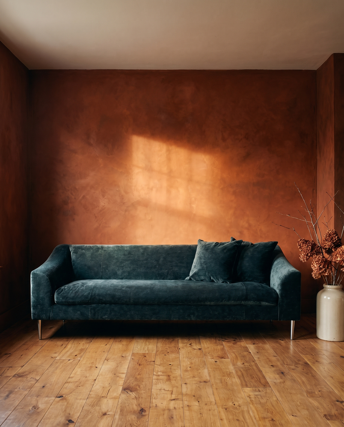 Vanguard Tess sofa in deep peacock crushed chenille against a glowing rust plaster wall, dried hydrangeas in a stoneware vessel