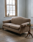 Taupe camelback sofa in a cool grey winter room with a snowy window and a tripod side table