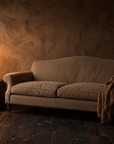 The Marcel camelback sofa by candlelight against a walnut plaster wall, with a rumpled umber linen throw