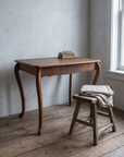 The oak desk in a cool grey plaster corner with old books, reading glasses and a wooden stool