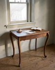 The oak desk under an old window in morning light with tea, letters and an open book