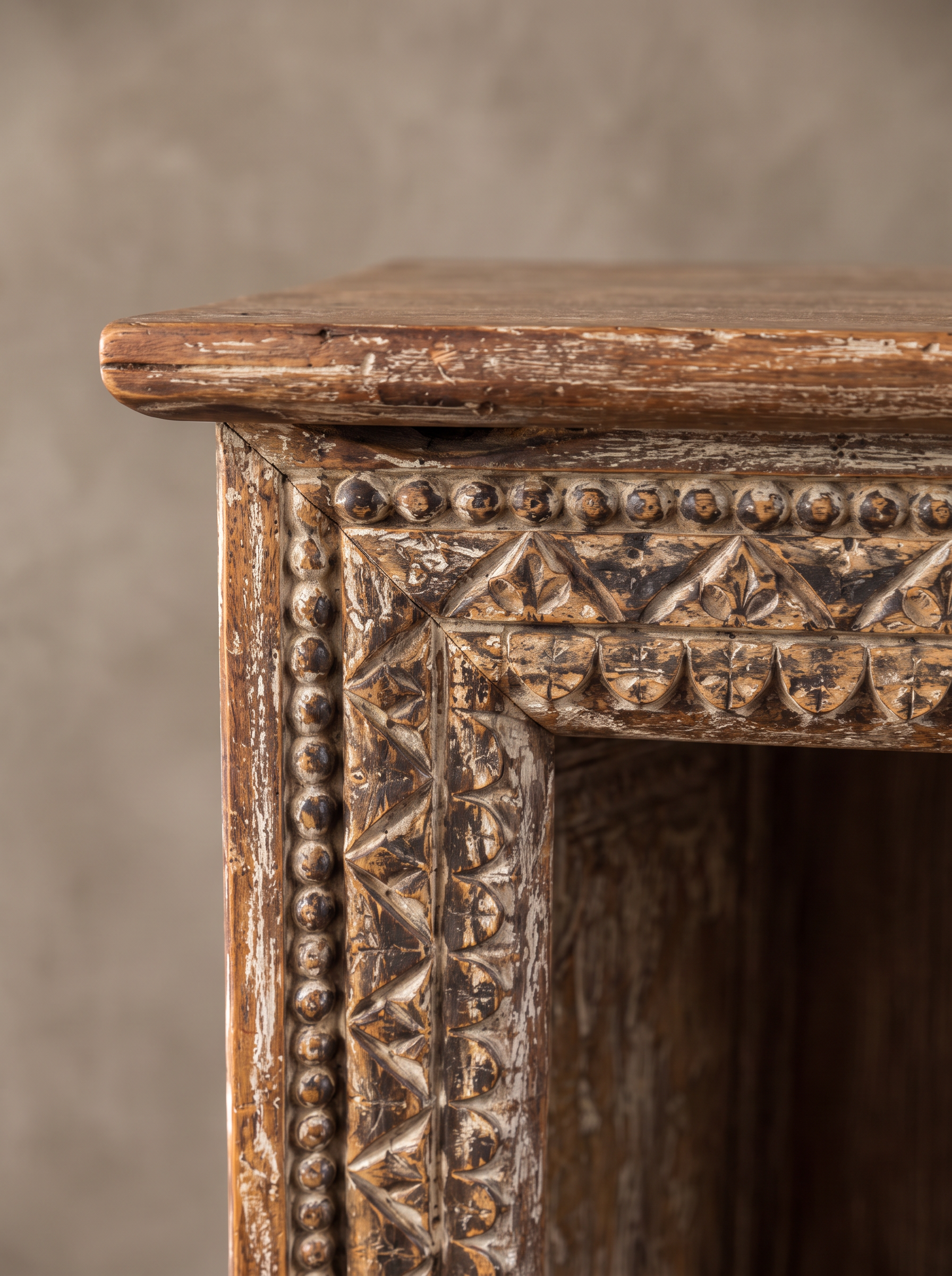 Close-up of the carved top corner: beads, triangles and scallops in a worn pale finish.