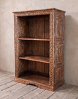 Carved Patina Bookcase, three-quarter view, against greige lime plaster on a wide bleached oak floor.