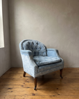 Powder blue crushed velvet tub chair with tufted back, three-quarter view in a plaster-walled room