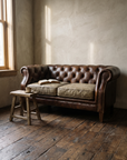 Leather chesterfield loveseat in morning window light with an open book and a stool with coffee