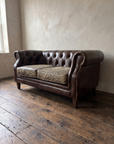 Three-quarter view of the tufted leather chesterfield loveseat with brass nailhead scroll arm