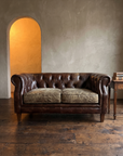 Leather chesterfield loveseat in a plaster salon with amber light through an arched doorway