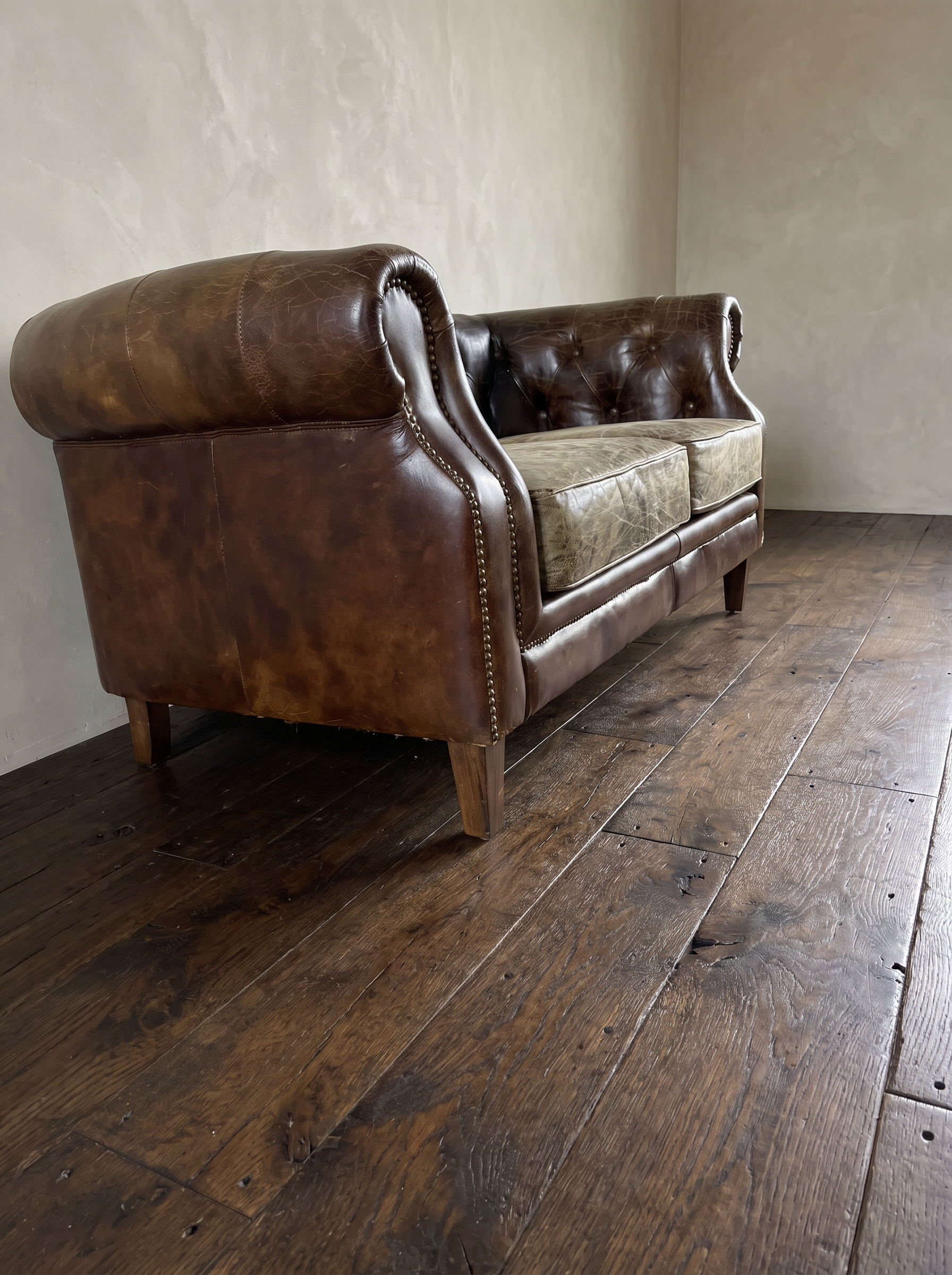 Low three-quarter view from the end of the leather chesterfield loveseat showing the arm roll and mottled patina