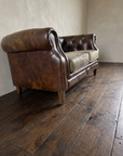 Low three-quarter view from the end of the leather chesterfield loveseat showing the arm roll and mottled patina