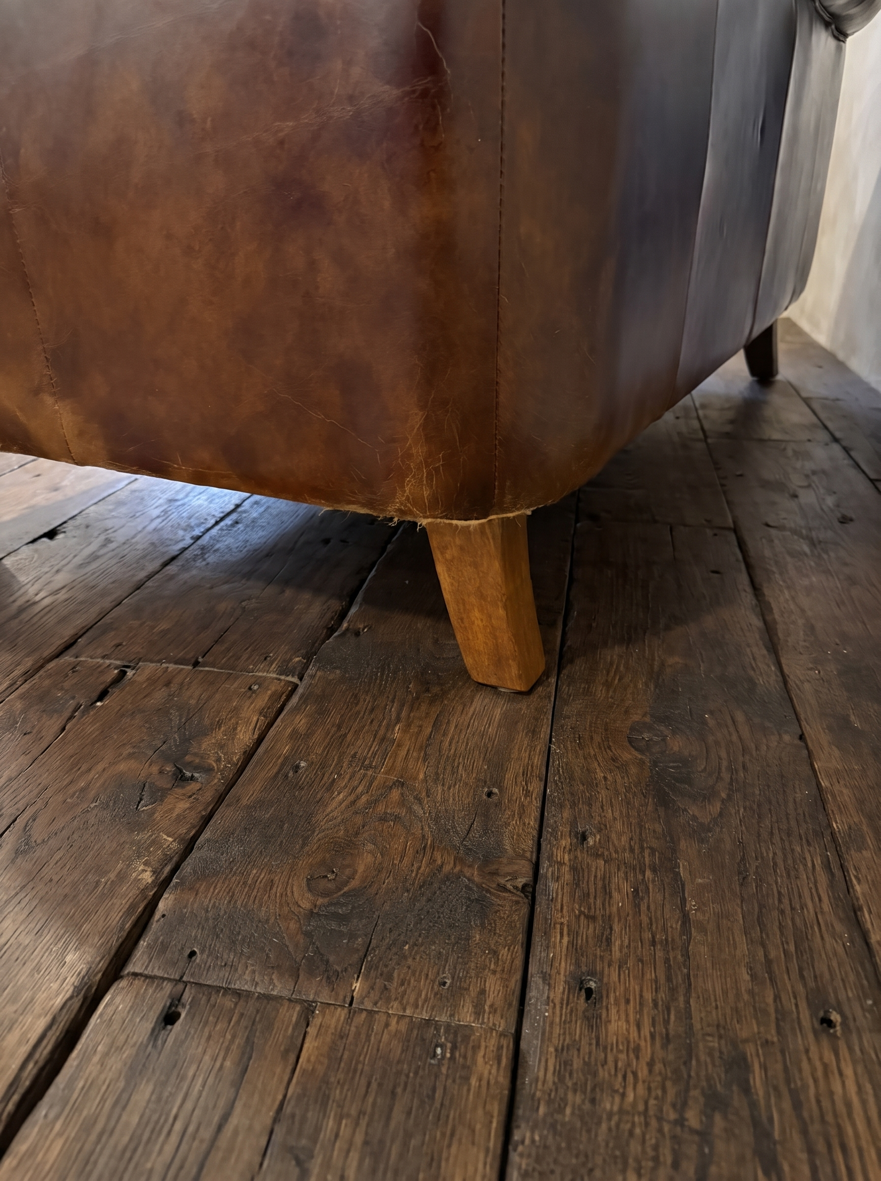 Detail of a lower back corner showing the stitched seam, honest wear and a tapered wood leg