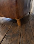 Detail of a lower back corner showing the stitched seam, honest wear and a tapered wood leg