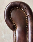 Close-up of the scroll arm curl traced in antique brass nailheads