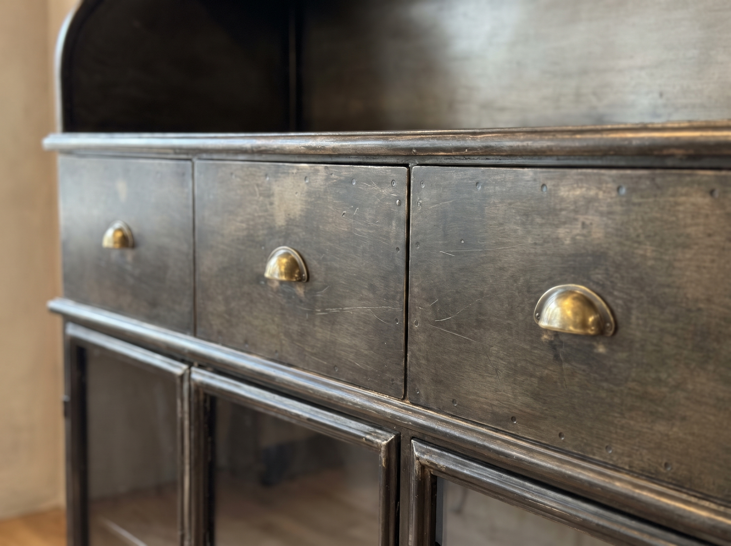Close-up of the three steel drawers with brass half-moon cup pulls and worn gunmetal patina