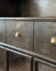 Close-up of the three steel drawers with brass half-moon cup pulls and worn gunmetal patina
