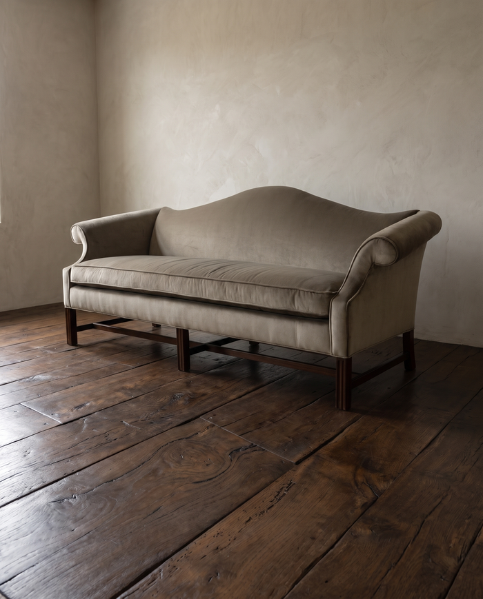 Vintage tan velvet camelback sofa with scroll arms and mahogany legs in a plaster room on a dark reclaimed oak floor