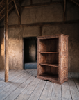 The bookcase in a tall old barn with clay plaster walls, high timber beams and grey plank floors.