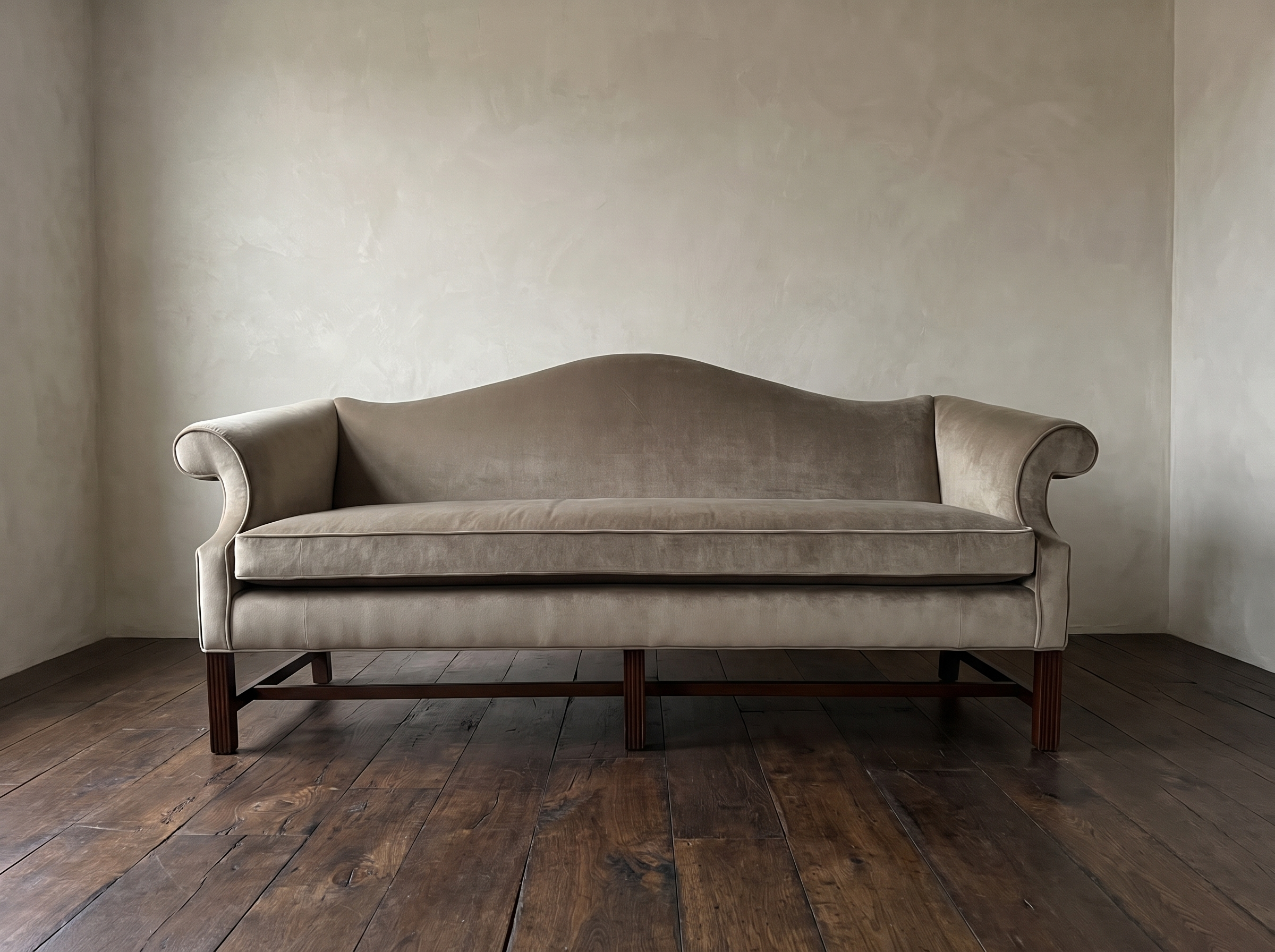 Straight-on front view of the tan velvet camelback sofa showing the bench cushion and six mahogany legs