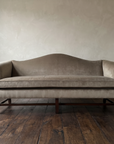 Straight-on front view of the tan velvet camelback sofa showing the bench cushion and six mahogany legs